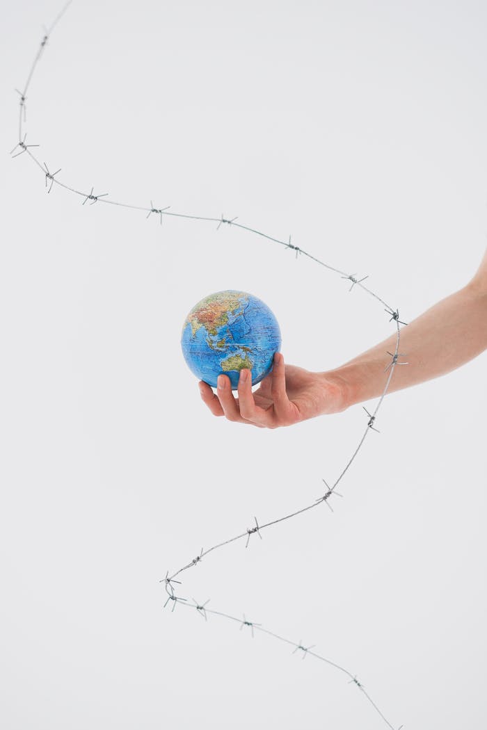 A hand holds a globe wrapped in barbed wire, symbolizing conflict and environmental challenges.
